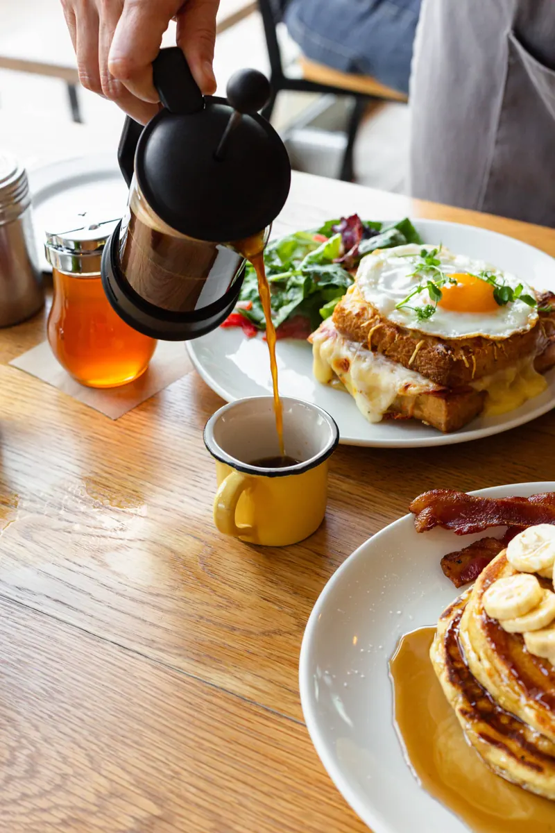 Café servido en french press junto a un Croque Monsieur con huevo y banana pancakes