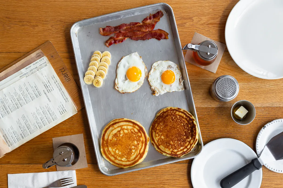 Desayuno en Merci: hot cakes, huevos estrellados, tocino y plátano servidos en charola