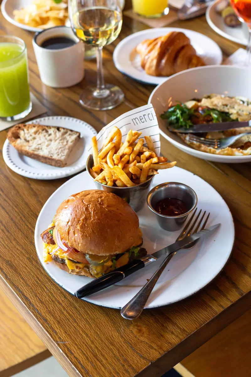 Mesa de brunch en Merci con hamburguesa, papas fritas, croissant y jugo verde