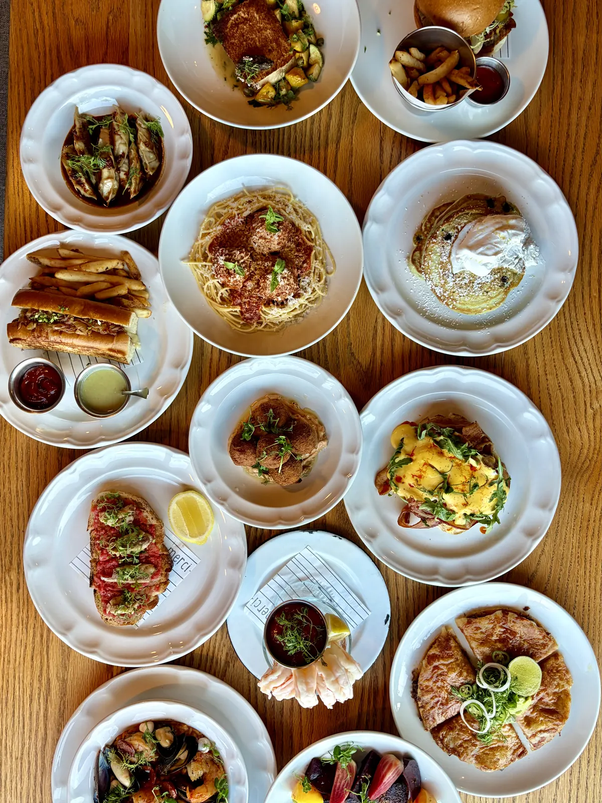 Mesa de Merci vista desde arriba con platillos de desayuno, comida y cena: gyozas de res, pasta, blueberry pancakes, huevos benedictinos, croquetas, sándwich de arrachera y queso birria