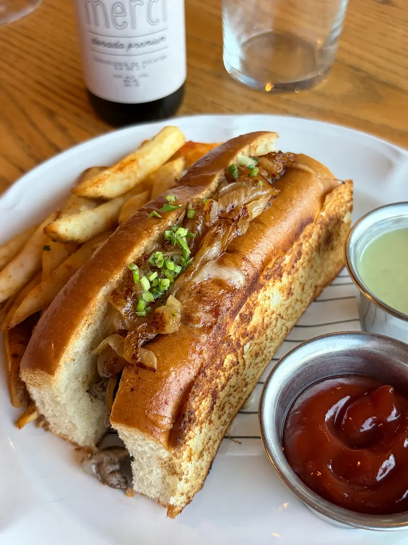 Sándwich de arrachera con cebolla caramelizada, salsa verde y papas a la francesa