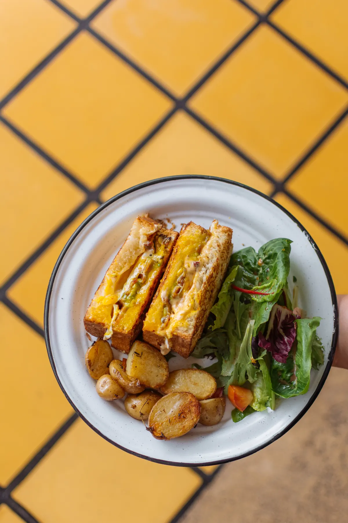 Sándwich tostado con papas y ensalada verde sobre mosaico amarillo